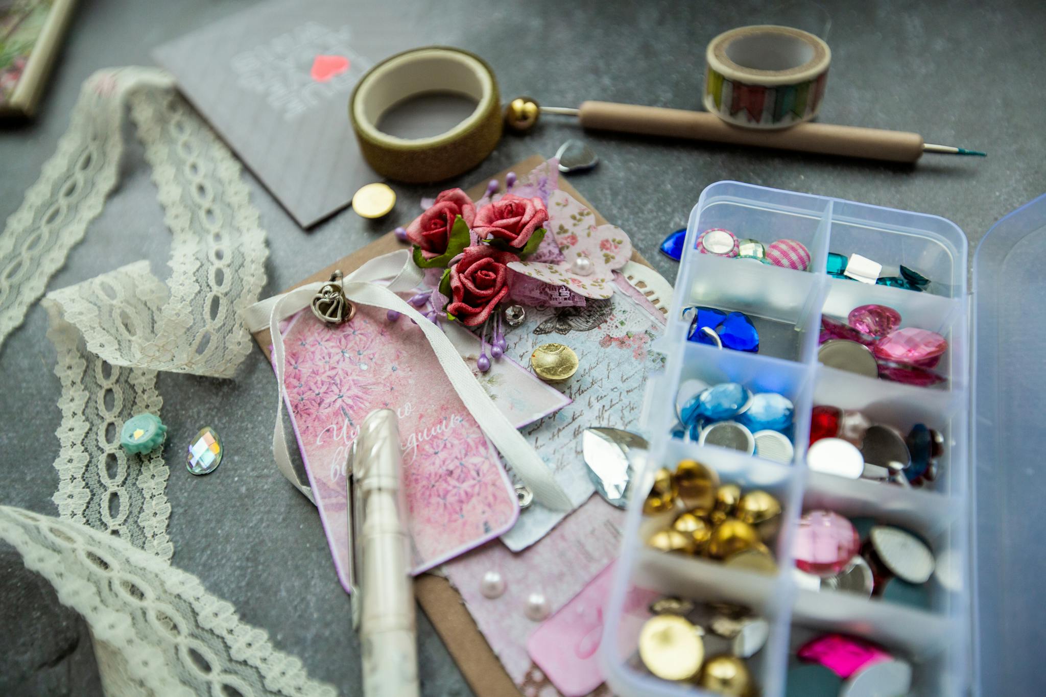 Handmade greeting card decorated with fancy stones and ribbon and placed on table with tools